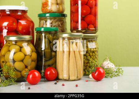 Gläser mit eingelegtem Gemüse und Zutaten auf einem hellen Tisch Stockfoto