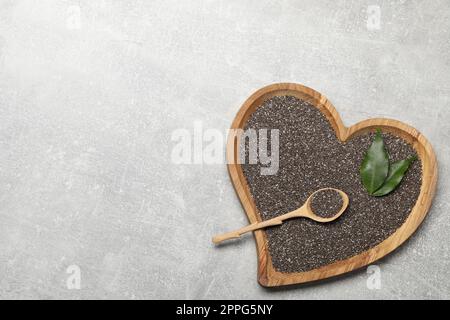 Chiasamen in Schüssel mit Löffel und grünen Blättern auf hellgrauem Tisch, Draufsicht. Platz für Text Stockfoto