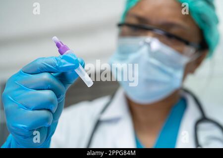 Ein asiatischer Arzt im PSA-Anzug zeigt ein positives Testergebnis mit dem Speichelantigen-Testkit zur Kontrolle des Covid19-Coronavirus im Krankenhaus. Stockfoto