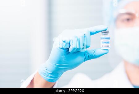 Wissenschaftler in Uniform, der eine Gesichtsmaske trägt und den Coronavirus-Impfstoff zeigt Stockfoto