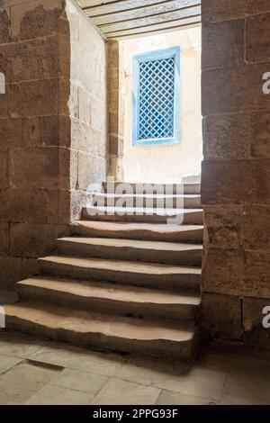 Eine alte, schmale dunkle Passage und Treppe führen zu einer kleinen Lobby im Freien mit blauen Holzfenstern Stockfoto