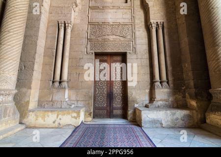 Alte Backsteinwand mit arabisch verzierten Holztüren, eingerahmt von steinreich verzierten zylindrischen Säulen Stockfoto