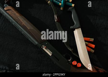 Waffe auf schwarzem Tuch: Messer, Gewehr, Patronen, Draufsicht. Draufsicht von Messer, Gewehr, Muscheln. Stockfoto