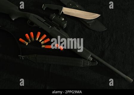 Waffe auf schwarzem Tuch: Messer, Gewehr, Patronen, Draufsicht. Draufsicht von Messer, Gewehr, Muscheln. Stockfoto