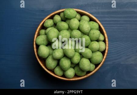 Leckere Wasabi-beschichtete Erdnüsse in der Schüssel auf blauem Holztisch, Draufsicht Stockfoto