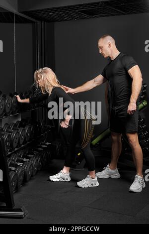 Fitnesstrainer führt Training für ein Mädchen mit Kurzhantel vor dem Spiegel durch Stockfoto