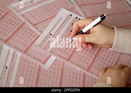 Ein Lotterielos ausfüllen. Eine junge Frau spielt im Lotto und träumt davon, den Jackpot zu gewinnen. Weibliche Handzeichen auf rotem Lotterielos Stockfoto
