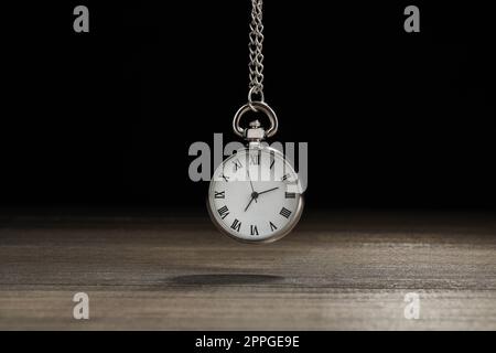 Wunderschöne Taschenuhr im Vintage-Stil mit silberner Kette auf schwarzem Hintergrund über dem Holztisch. Hypnose-Sitzung Stockfoto