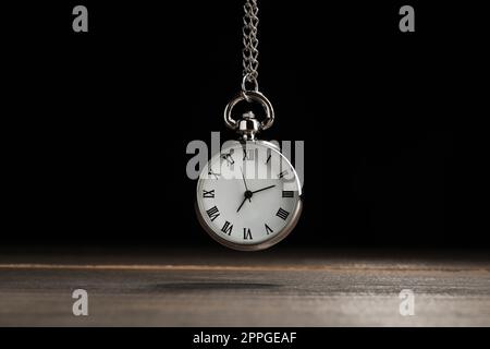 Wunderschöne Taschenuhr im Vintage-Stil mit silberner Kette auf schwarzem Hintergrund über dem Holztisch. Hypnose-Sitzung Stockfoto