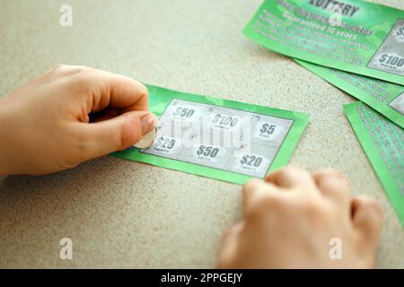Nahaufnahme der Silbermünze in der Hand eines Spielers, der eine gefälschte Lotteriekarte kratzt. Lotterie, Glücksspiel, Kratzkarten-Lotterie Stockfoto