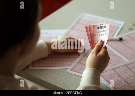 Ein Lotterielos ausfüllen. Eine junge Frau hält das Lotterielos mit einer kompletten Zahlenreihe auf dem Hintergrund der leeren Blätter. Stockfoto