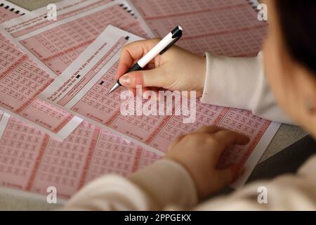 Ein Lotterielos ausfüllen. Eine junge Frau spielt im Lotto und träumt davon, den Jackpot zu gewinnen. Weibliche Handzeichen auf rotem Lotterielos Stockfoto