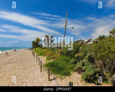 Fernblick auf die sonnige und tropische blaue Wasserküste mit Menschen, Vegetation, Booten und Gebäuden im Hintergrund von über dem Wasser aus gesehen. Stockfoto