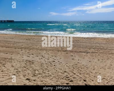 Fernblick auf die sonnige und tropische blaue Wasserküste mit Menschen, Vegetation, Booten und Gebäuden im Hintergrund von über dem Wasser aus gesehen. Stockfoto