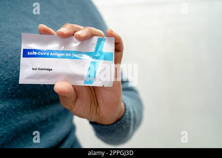 Ein asiatischer Arzt im PSA-Anzug zeigt ein positives Testergebnis mit dem Speichelantigen-Testkit zur Kontrolle des Covid19-Coronavirus im Krankenhaus. Stockfoto