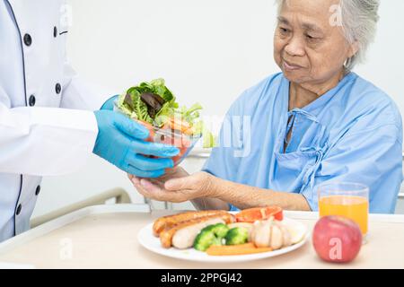 Asiatische Seniorin oder ältere Frau Patientin isst Frühstück und Gemüse gesunde Lebensmittel mit Hoffnung und glücklich während sie im Krankenhaus sitzen und hungrig im Bett. Stockfoto