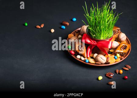 Novruz Tischdekoration, Weizengras, Baklava Gebäck und Nüsse auf Schwarz. Arabischer Feiertag von Nowruz, Frühlingsfeier, Kopierraum. Stockfoto