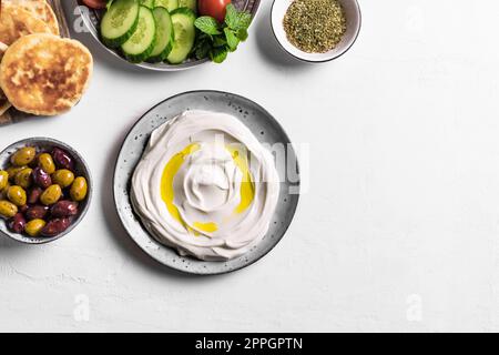Lab−Joghurt-Frischkäse mit Olivenöl, Zaatar, Oliven, Gemüse und Pita-Brot auf weißem Tisch, Kopierbereich. Traditionell arabisch oder nahöstlich Stockfoto