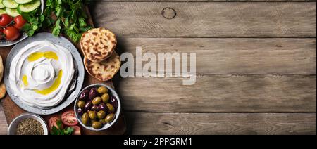Lob-Joghurt-Frischkäse mit Olivenöl, Zaatar, Oliven, Gemüse und Pita-Brot auf Holzhintergrund, Kopierbereich, Banner. Traditionell arabisch oder Stockfoto