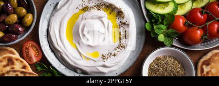 Lob Joghurt Frischkäse mit Olivenöl, Zaatar, Oliven, Gemüse und Pita Brot, Banner. Traditionelles arabisches, griechisches oder nahöstliches Frühstück mit Stockfoto