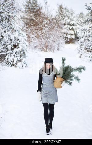 Ein junges Mädchen in silbernem Kleid und Hut steht mit dem Rücken inmitten eines wunderschönen Winterwaldes. Stockfoto