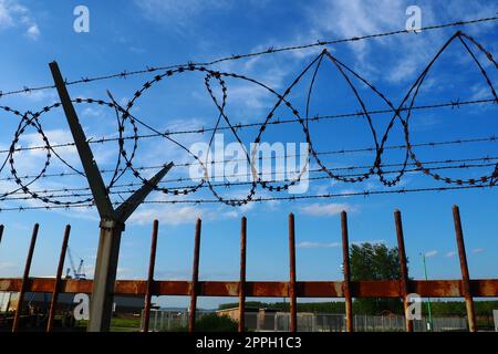 Stacheldraht am blauen Himmel. Stacheldraht ist ein Draht oder ein schmaler Metallstreifen mit scharfen Spitzen. Vorrichtung der Barrieren. Das Konzept der Freiheit, des Eigentumsschutzes, der Gewalt, der Inhaftierung Stockfoto