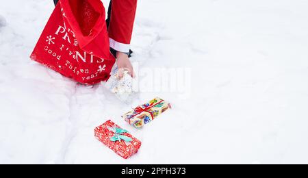 Bannermann als Weihnachtsmann gekleidet sammelt Geschenke in einem verschneiten Wald im Schnee, bunte Boxen mit Geschenken. Stockfoto