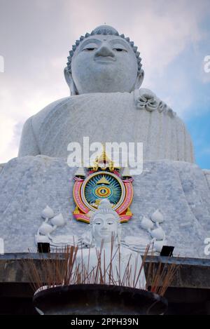 Riesige Marmor statue des Sitzenden Buddha in Phuket, Thailand, als "Big Buddha" bekannt. Eine kleinere Statue mit Weihrauch Angebote im Vordergrund. Stockfoto