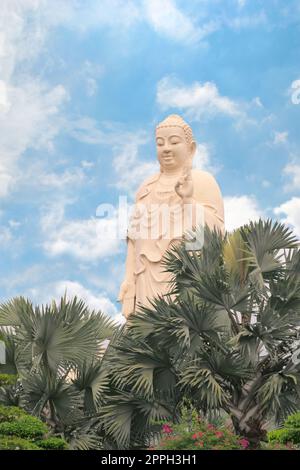 Stehende buddha-Statue am Vinh Trang Tempel, in der Nähe von My Tho, Vietnam. Palmen und Garten im Vordergrund. Stockfoto