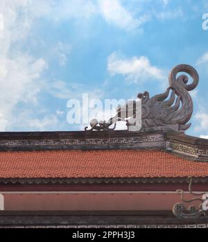 Drachenskulptur auf dem Dach eines kinen buddhistischen Tempels gegen einen blauen Himmel mit spärlichen Wolken. Stockfoto