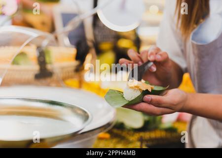 Eine Verkäuferin, die klebrigen Reis mit Vanillesauce zubereitet, verpackt in Bananenblätter. Stockfoto