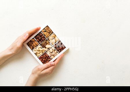 Junge Frau, die eine Kiste mit anderen Nüssen hält, Nahaufnahme. Nahaufnahme, Kopierbereich, Draufsicht, flach liegend. Walnuss, Pistazien, Mandeln, Haselnüsse und Cashews. Stockfoto