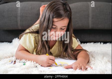 Fröhliches kleines Mädchen, das auf der Bodenzeichnung liegt. Stockfoto