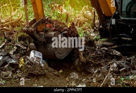 Baggerlader Graben von Erde auf der Baustelle. Schaufel mit Baggerladerboden zum Graben. Roden und Roden. Bagger auf Straßenbaustellen. Erdbewegungsmaschine. Ausgrabungsfahrzeug. Erschließung von Grundstücken. Stockfoto