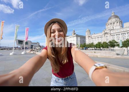 Tourismus in Liverpool, Großbritannien. Wunderschöne junge Frau macht Selfie vor Pier Head mit „The Three Graces“ im Stadtzentrum von Liverpool, England. Stockfoto