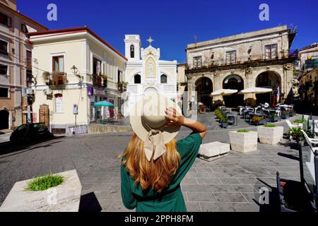 Besuch in Kalabrien in Italien. Rückansicht einer jungen Frau mit Strohhut, die im historischen Zentrum von Pizzo Calabro, Italien, spazieren geht. Stockfoto