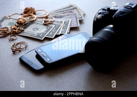 Viele teure goldene Schmuckringe, Ohrringe und Halsketten mit vielen US-Dollar-Scheinen in der Nähe von Smartphones und digitalen spiegelreflexkameras. Pfandhaus Stockfoto