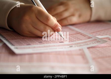 Ein Lotterielos ausfüllen. Eine junge Frau spielt im Lotto und träumt davon, den Jackpot zu gewinnen. Weibliche Handzeichen auf rotem Lotterielos Stockfoto