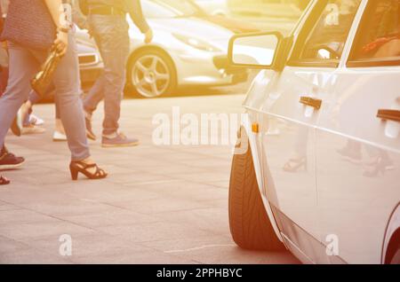 Diagonalansicht eines weißen, glänzenden Autos, das auf einem Quadrat grauer Fliesen steht Stockfoto