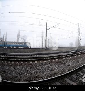 Der ukrainische Vorstadtzug rast an einem nebligen Morgen entlang der Eisenbahn. Fischaugenfoto mit erhöhter Verzerrung Stockfoto