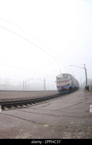 Der ukrainische Vorstadtzug rast an einem nebligen Morgen entlang der Eisenbahn. Fischaugenfoto mit erhöhter Verzerrung Stockfoto