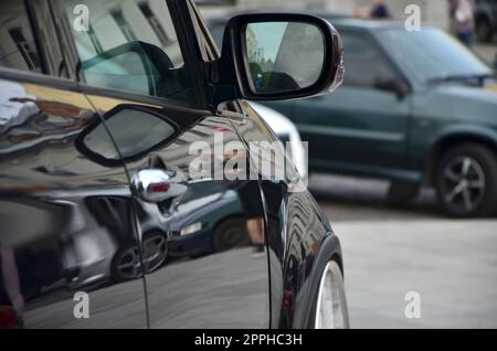 Diagonalansicht eines schwarz glänzenden Autos mit weißen Rädern, das auf einem Quadrat grauer Fliesen steht Stockfoto