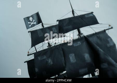 Flagge Jolly Roger Skull und Knochen des Piratenschiffs Modell Schwarze Perle aus Sperrholz, verschwommene, geflickte Segel und Seile Stockfoto