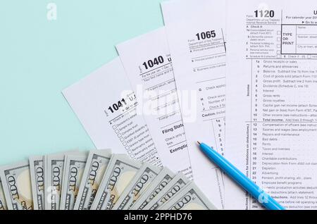 Die Steuerformulare liegen fast 100-Dollar-Scheine und ein blauer Stift auf hellblauem Hintergrund. Einkommensteuererklärung Stockfoto