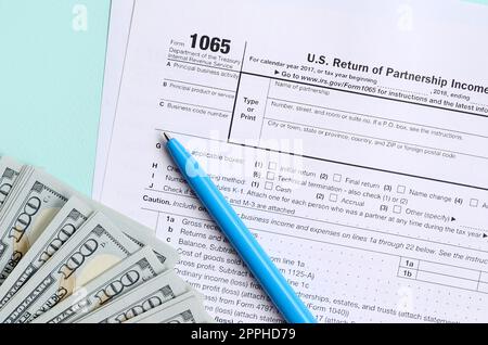 Das Steuerformular für 1065 liegt in etwa 100-Dollar-Scheinen und einem blauen Stift auf hellblauem Hintergrund. US Return for Parentship Income Stockfoto