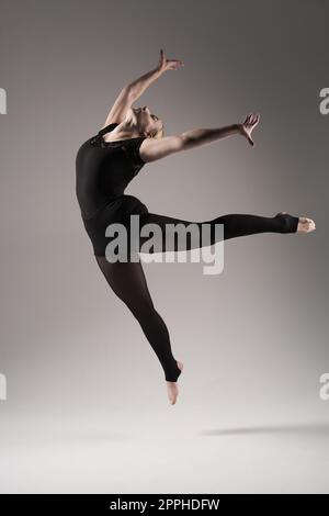 Balletttänzerin Frau schwarzes Kleid auf grauem Hintergrund, Ballerina posiert und zeigt ihre Flexibilität auf grauem Hintergrund im Studio Stockfoto