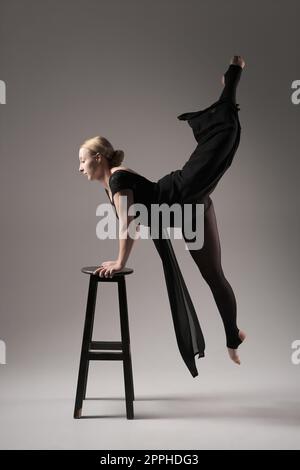 Ballerina Dancing with Silk Fabric, Modern Ballet Dancer in flatterndem, winkenden Tuch, grauer Hintergrund mit schwarzem Stuhl Stockfoto