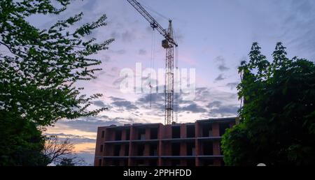 Baukran am Himmelshintergrund. Baustelle. Industriekräne und Bausilhouetten über der Sonne bei Sonnenaufgang. Stockfoto