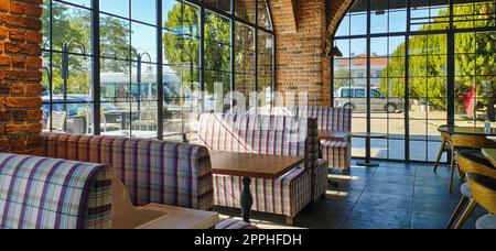 Bar mit Theke, Hockern und quadratischen Tischen. Ein leerer Innenausschnitt der Cafeteria. Große Fenster lassen Licht herein. Konzept des Trinkens Stockfoto