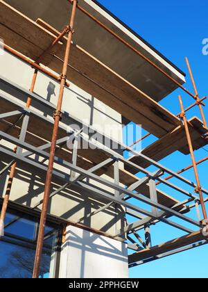 Gerüste auf einem neuen einstöckigen Haus. Die Fassade funktioniert. Geschäftsgebäude. Flaches privates Gebäude. Die Wand eines Gebäudes putzen. Ladenbau. Produktionsstrukturen für Metall. Stockfoto